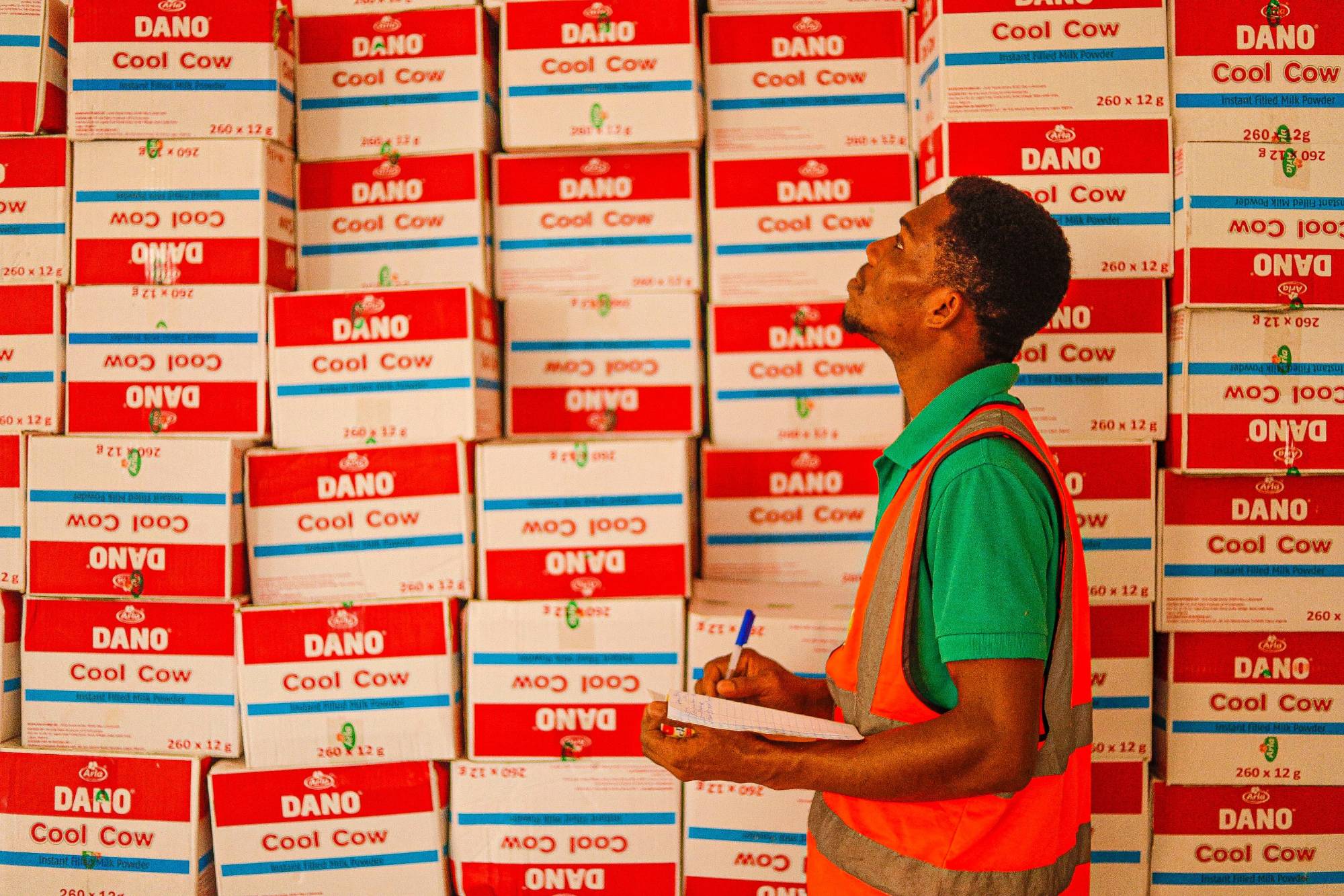 Warehouse staff member in a high-visibility vest counting stacked cartons of milk powder